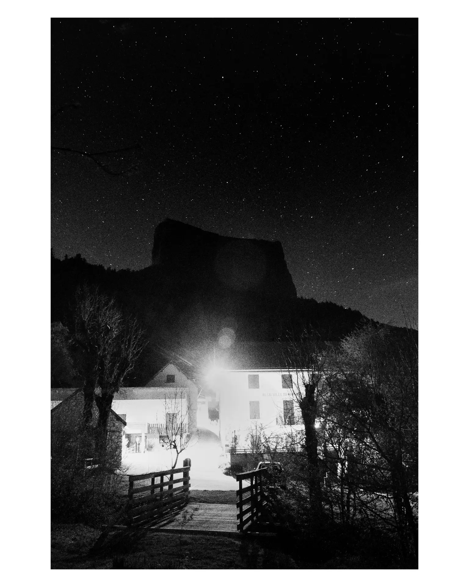 Black-and-white night photograph of stars above a lit building