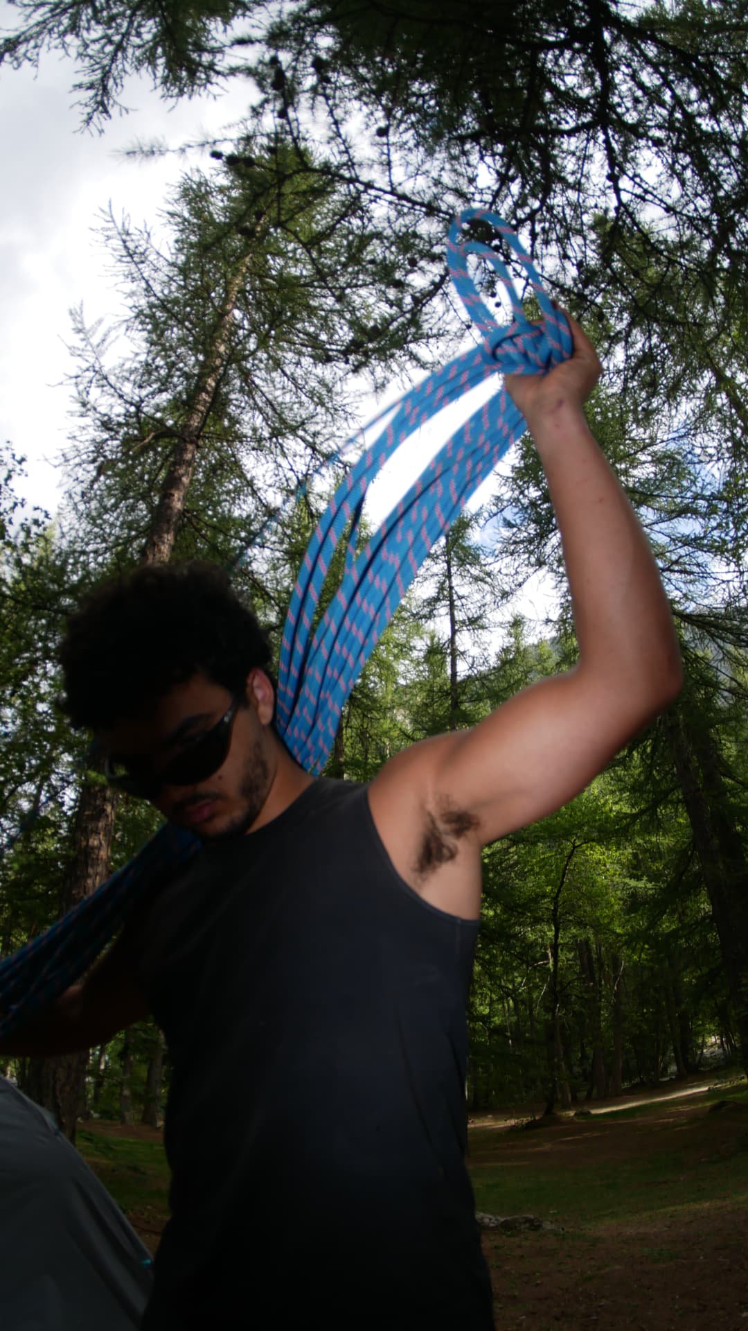 A climber holding a coiled blue rope overhead in an alpine forest