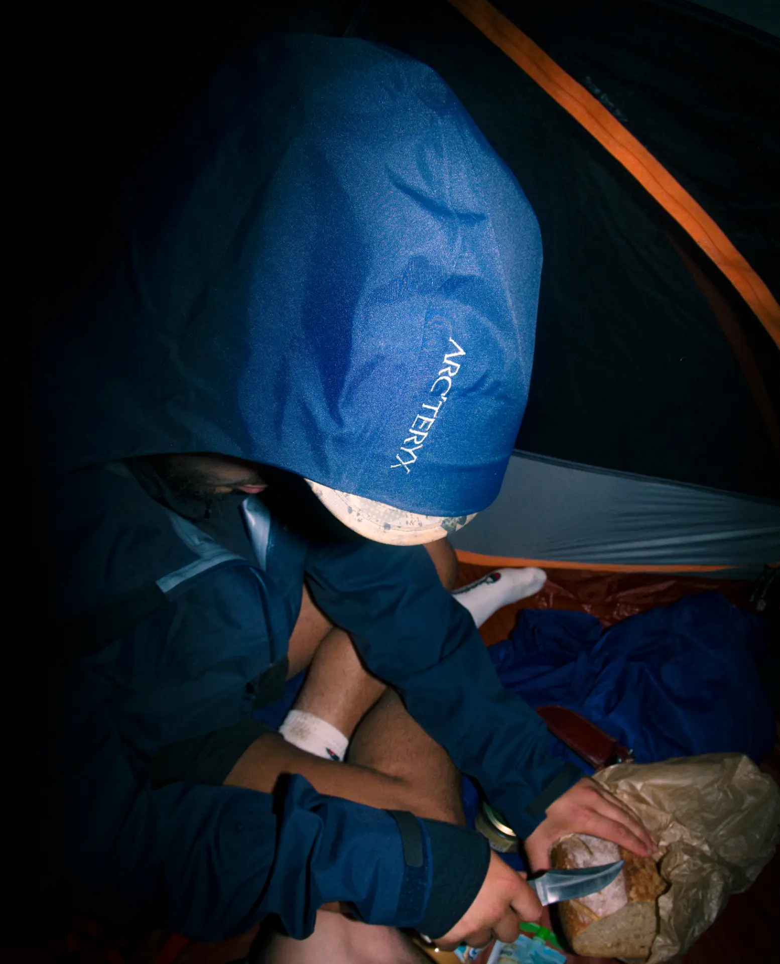 Flash photograph inside a tent of a person in a blue jacket with bread