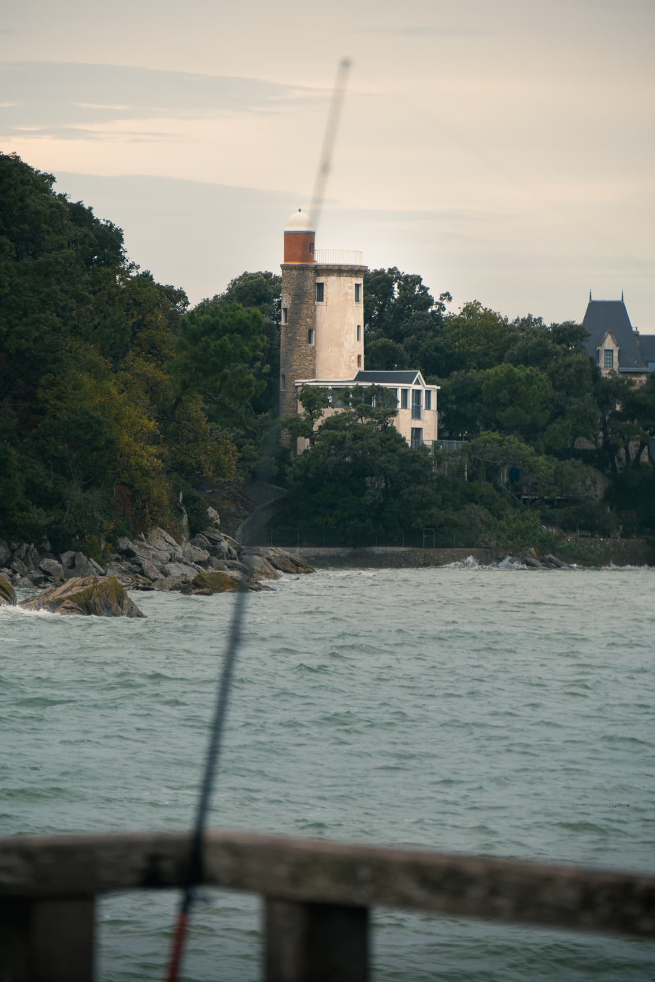 A coastal lighthouse seen across the water with a blurred fishing rod in the foreground