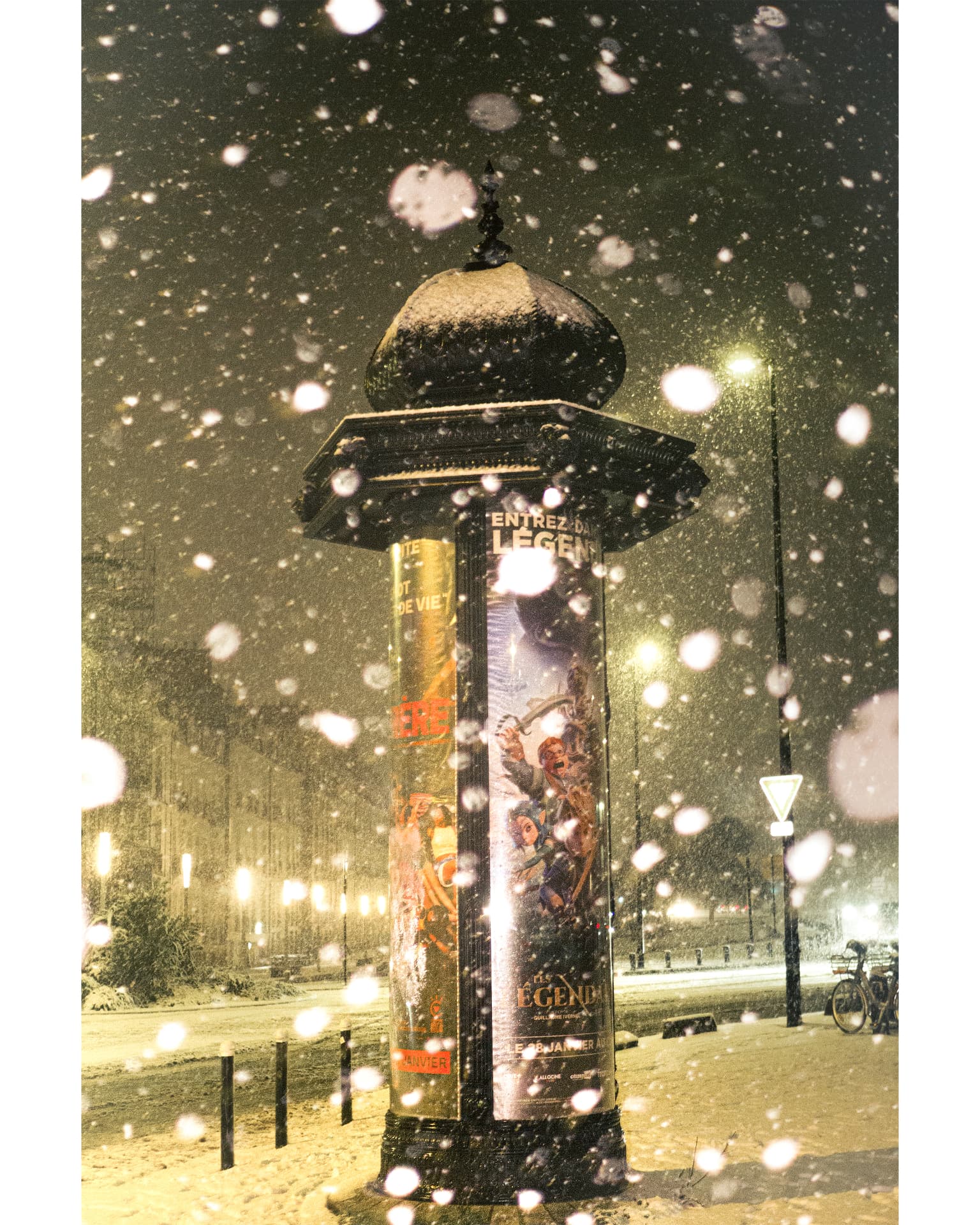 A snow-covered advertising column at night through falling snowflakes