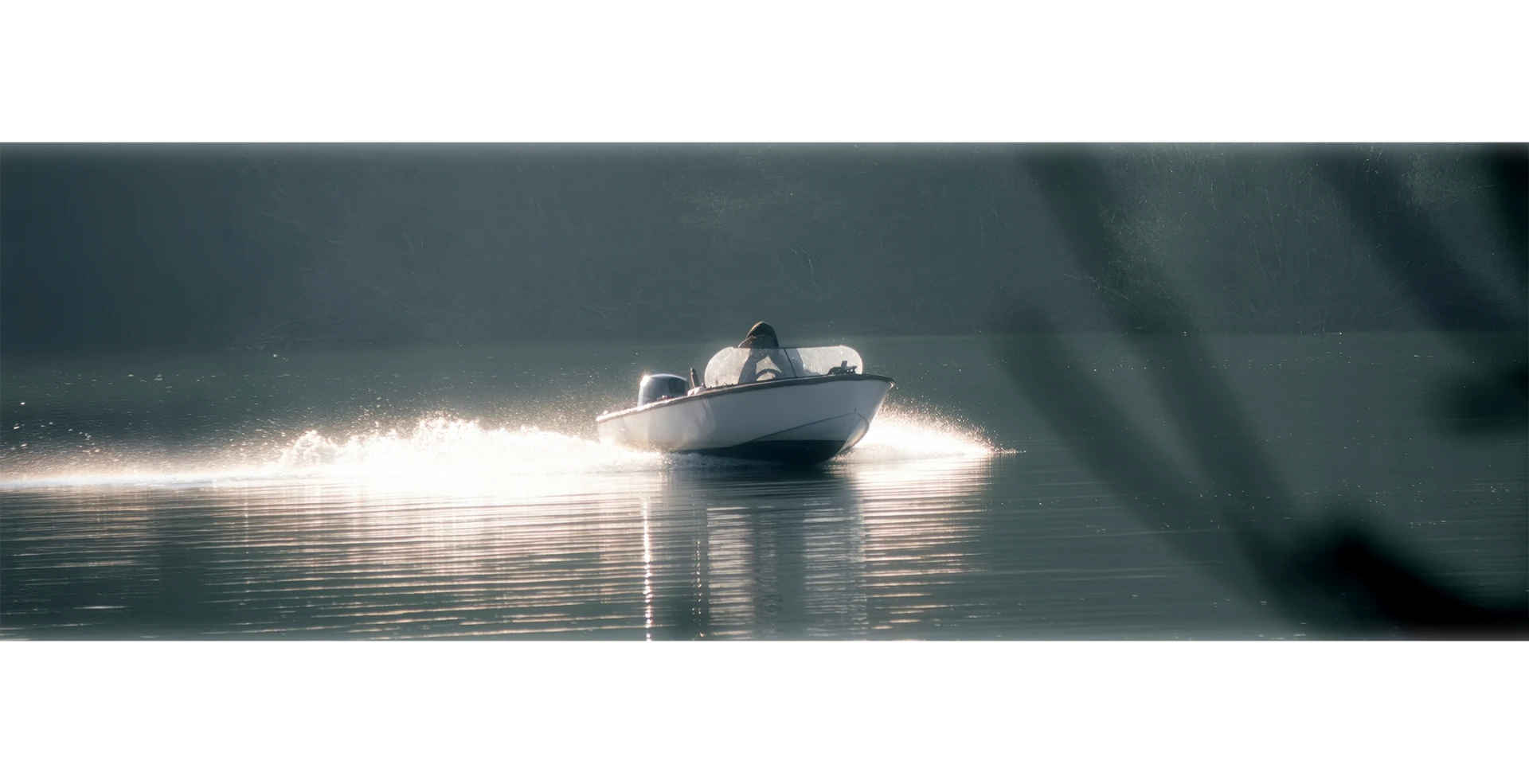 A small motorboat crossing calm water in backlight